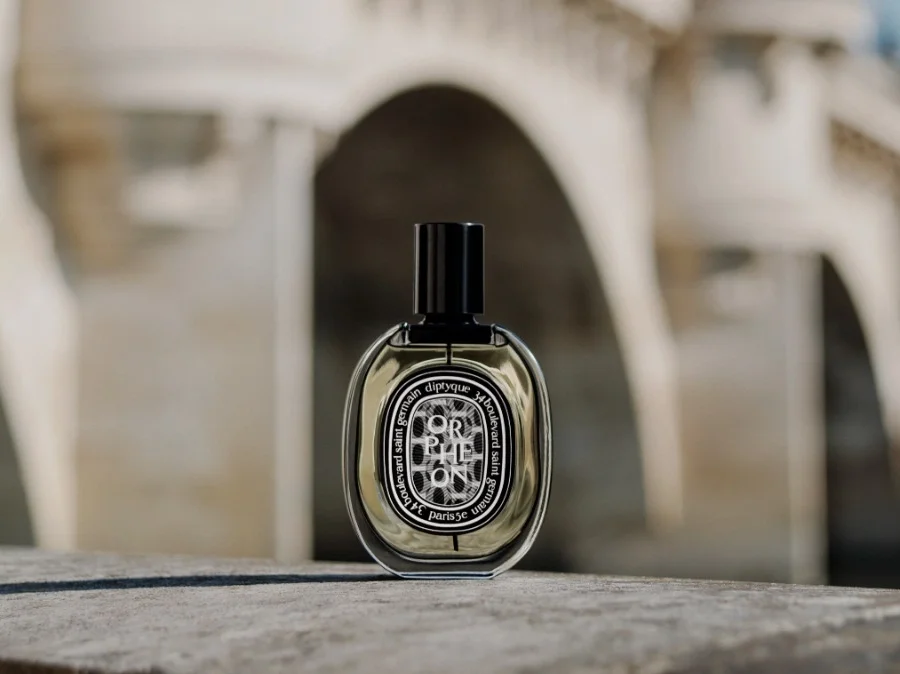 Close-up of Diptyque Orphéon perfume bottle surrounded by positive customer reviews highlighting its unique scent and craftsmanship