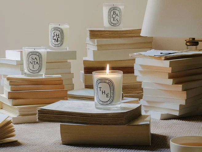 Four Diptyque candles displayed on a stack of books, emphasizing the luxury and elegance of the brand.