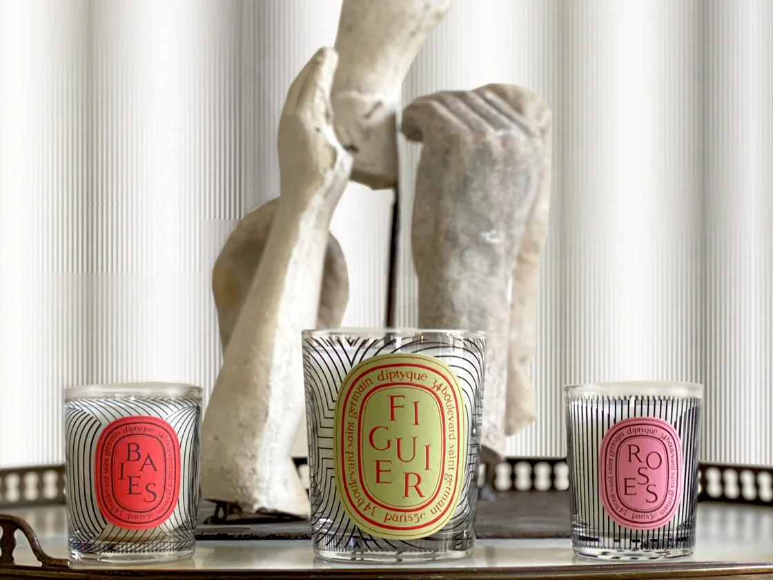 Three Diptyque candles, including Baies, Roses, and Feu de Bois, elegantly displayed on a coffee table.