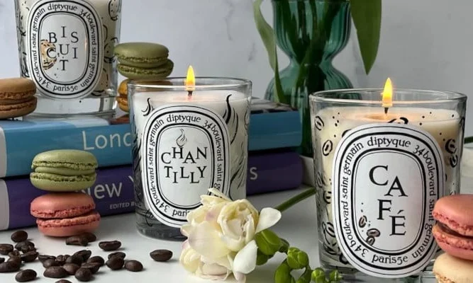 Minimalist display of Diptyque candles and perfumes on a white table.