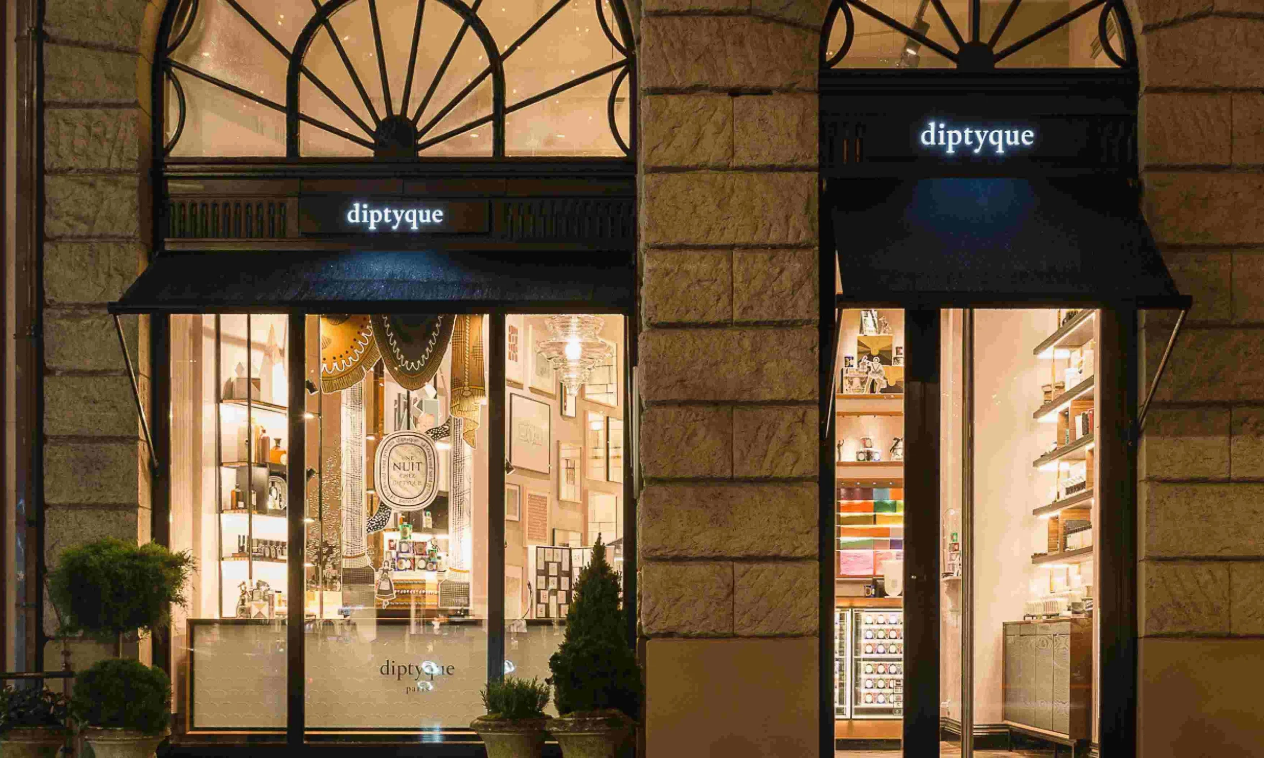 Close-up of Diptyque candles and perfume bottles in soft lighting.